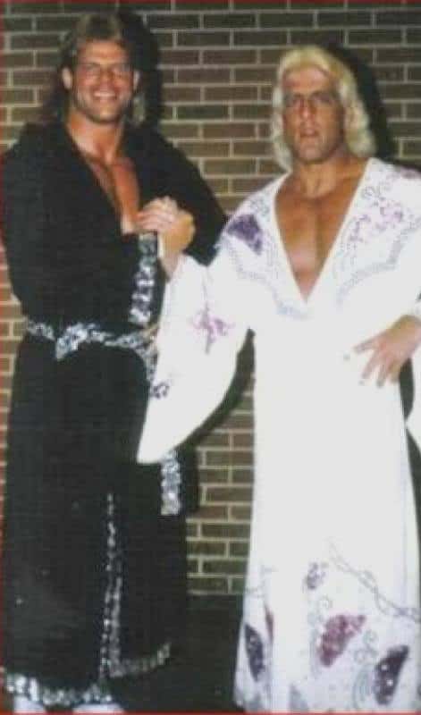 Lex Lugar and Ric Flair clasping hands both wearing sequin robes