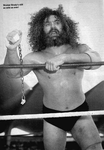 Bruiser Brody with wild hair leaning on the ring ropes holding a metal chain