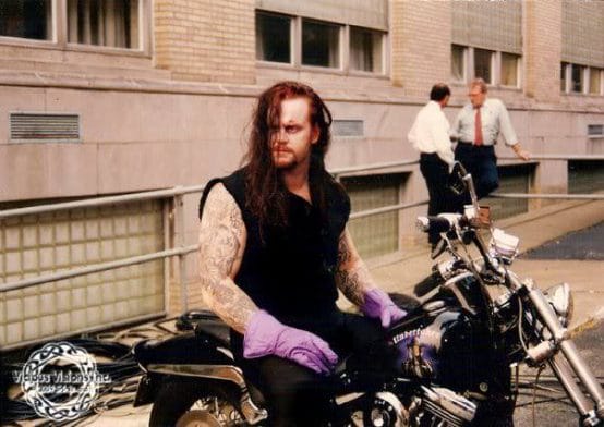 The undertaker backstage sitting on one of his motorcycles with purple gloves on.