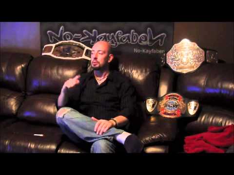 Undertaker | 18 Stories Showing Who the Real Deadman Was Justin Credible sitting on a black leather sofa in jeans and a black shirt surrounded by his belts.