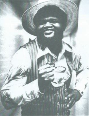 Norvell Austin, founding member of The Midnight Express, in a straw hat, striped vest and satin shirt holding glasses