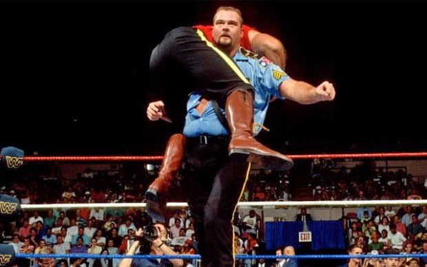 Big Boss Man, Ray Traylor, in his signature corrections officer uniform, with a wrestler hoisted over his shoulder
