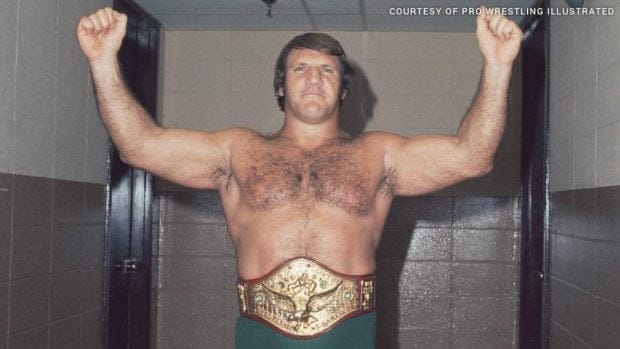 Bruno Sammartino in his title belt showing off as victor with arms in the air doing a strong man pose