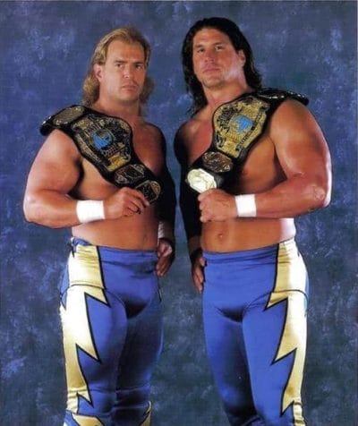 The New Midnight Express (Bob Holly and Bart Gunn) Tag Team in blue wresting pants with lightning bolts down the sides with title belts on their shoulders