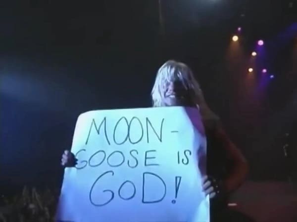 Chris Jericho on wrestlers outside the ring is pictured as lead singer of Fozzy holding a poster that says Moon-Goose is God!
