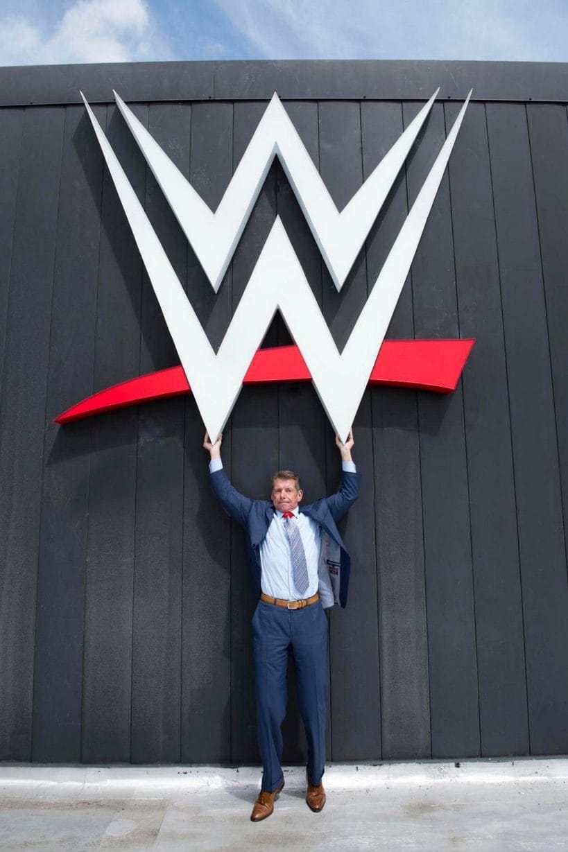 Vince McMahon stands proudly underneath the current WWE logo