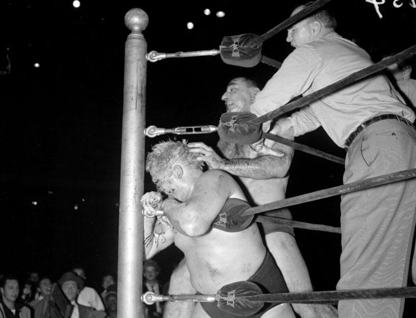 An outraged Antonino Rocca bangs Dr. Jerry Graham's head against the ring post as referee Danny Bartfield tries to intervene.